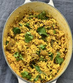 a large pot filled with yellow rice and meat covered in cilantro leaves on top of a blue cloth