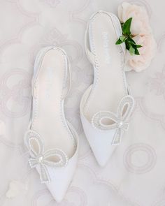 a pair of white shoes sitting on top of a bed next to a pink flower