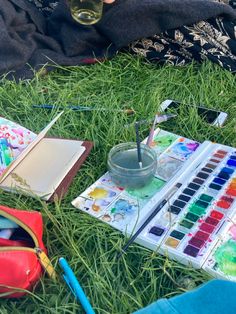 a person sitting in the grass with their laptop and watercolors next to them