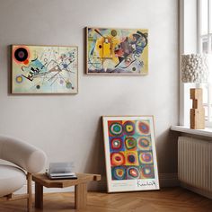 two paintings hang on the wall next to a chair and coffee table in a living room