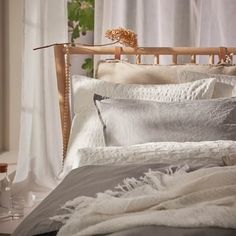 a bed with white linens and pillows in front of a curtained window,