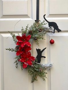 a christmas wreath on the front door with a black cat and poinsettis