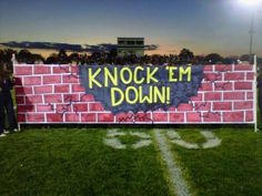 a brick wall with the words knock em down painted on it in front of a football field