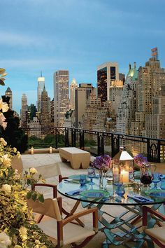 a glass table with candles on it in front of a cityscape and flowers