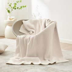 a white blanket sitting on top of a rug next to a vase filled with flowers