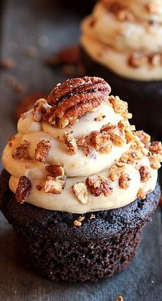 chocolate cupcakes with white frosting and pecans on top, sitting on a black surface