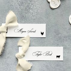 two place cards with bows on them sitting next to some waxed paper and buttons