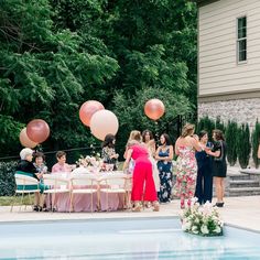 a group of people standing around a pool with balloons in the shape of heart shapes