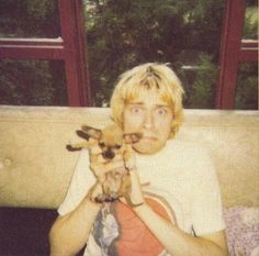 a man sitting on a couch holding two puppies in front of his face and looking at the camera