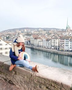 two people sitting on a stone wall looking at the water and buildings in the background