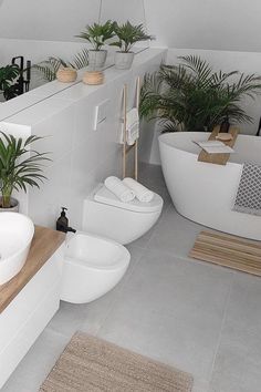 a white bathroom with plants in the bathtub and on the counter, along with two sinks