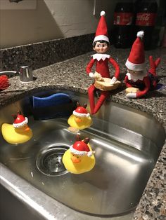 two elfs sitting on top of a sink next to rubber ducks