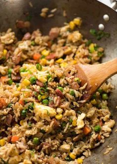 rice and vegetables being cooked in a wok with a wooden spoon on the side