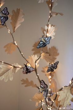 a branch with some butterflies on it and lights strung from the branches around it in front of a wall