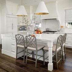 a large kitchen with white cabinets and wooden flooring, two pendant lights hanging over the island