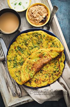 an omelet is on a plate next to two cups of coffee and spoons