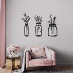 three vases with flowers are hanging on the wall above a pink chair and side table