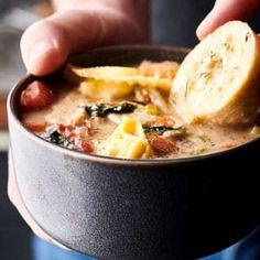 a person is holding a bowl of soup with some bread on the side and their hand reaching for it