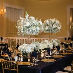 the table is set with black linens and gold place settings, white flowers in centerpieces