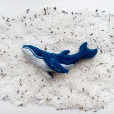 a blue and white stuffed whale laying on top of some seaweed in the sand