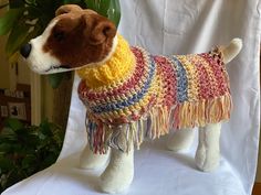 a stuffed dog wearing a colorful sweater on top of a white table next to a potted plant