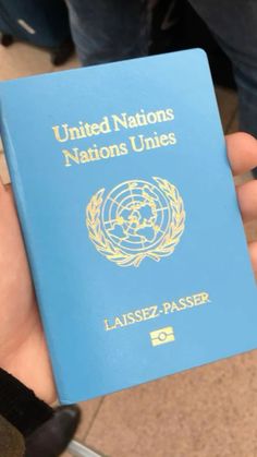 a person holding up a blue passport in their hand with the united nations logo on it