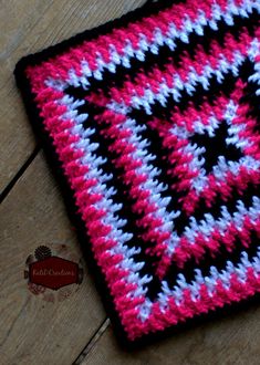 a crocheted square is sitting on a wooden floor with a red, white and blue design