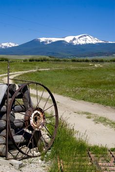 an old wagon sitting on the side of a dirt road in front of a mountain