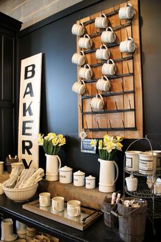 there are many cups and mugs on the counter in this room with a sign that says baker's