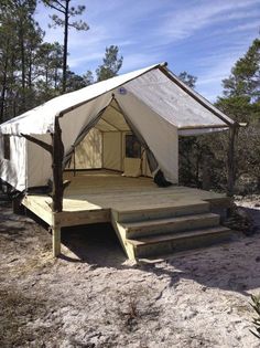 a white tent with steps leading up to it in the middle of some dirt and trees