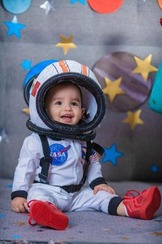 a baby wearing an astronaut's helmet sitting on the ground