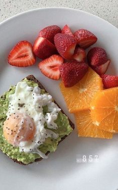 an egg and avocado toast with strawberries are on a plate next to sliced oranges