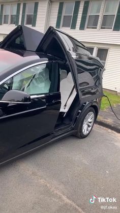 an electric car parked in front of a house with its doors open and it's hood up