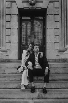 a man and woman sitting on steps in front of a building with their arms around each other