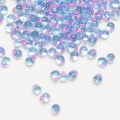 blue and pink beads are scattered on a white surface with water droplets in the foreground