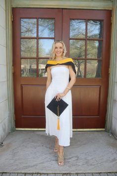 a woman standing in front of a door wearing a white and yellow dress with black accents