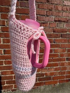 a crocheted pink bag hanging on a brick wall next to a plastic cup