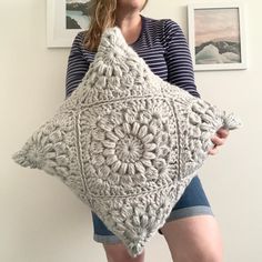 a woman holding a crocheted pillow in front of two pictures on the wall