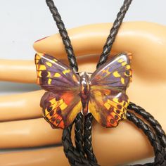 This eye catching lithographed tin butterfly bolo tie is perfect for a man or for a woman who wishes to make a statement. The butterfly is  mostly brown with touches of yellow and orange. It looks real.     The bolo slide measures 1 1/2 inches tall and 1 3/4 inches  wide and is placed on a 36 inch long black leather string tie with golden brass metal end caps. This was made in our our own shop, Rockin' JK.  We will send this to you in a lovely gift box for that special presentation. If you like Vintage Black Bolo Ties For Gift, Vintage Black Bolo Ties As Gift, Black Bolo Tie With Adjustable Cord As Gift, Unique Adjustable Bolo Tie For Gift, Unique Adjustable Bolo Ties For Gifts, Handmade Bolo Ties As Unique Gifts, Adjustable Brown Bolo Ties For Gifts, Adjustable Brown Bolo Ties As Gift, Handmade Gold Bolo Tie For Gift