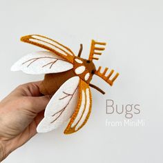 a hand holding a small insect made out of felt