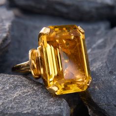 This bold and classic circa 1940s retro ring features one (1) emerald cut natural citrine set into a four-prong setting. The ring has curved shoulders for extra dimension.  It measures 21.0mm at the top, rises 13.4mm above the finger, and tapers to 1.8mm wide by 1.6mm thick at the base of the shank. It is crafted in 14k yellow gold, with its light patina intact, and is currently a size 5.5. Classic Yellow Topaz Ring With Emerald Cut, Classic Yellow Emerald Cut Topaz Ring, Classic Emerald Cut Yellow Topaz Ring, Yellow Gemstone Jewelry, Antique Engagement Rings Sapphire, Estate Jewelry Rings, Wedding Ring Diamond Band, Clothing Tips, Yellow Style