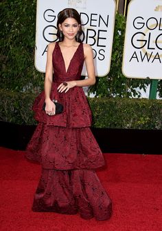 a woman in a red dress on the red carpet at an awards event with her purse