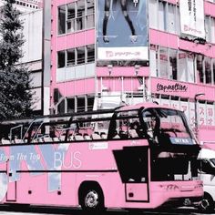 a pink bus is parked in front of a tall building with an advertisement on it