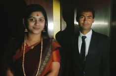 a man and woman standing next to each other in front of an elevator with the door open