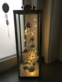 a lighted display case with ornaments and lights on the bottom, in front of a window