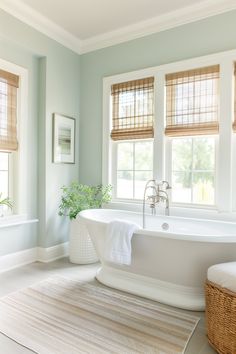 a white bath tub sitting in a bathroom next to two windows with blinds on them