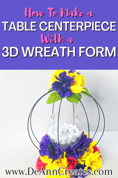 This pin shows a table centerpiece made with a 3D wreath form. It has colorful artificial flowers around the base and on top of it. It has a candle holder in the center filled with vase filler and a battery-operated candle. Dollar Tree Ring Centerpiece, Dollar Tree 3d Round Wreath Form Ideas, Dollar Tree 3d Wreath Form Ideas