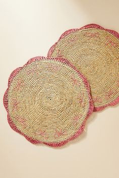 two round placemats with pink trim on white table top next to each other