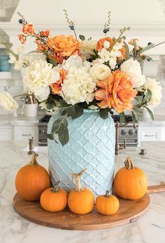 a blue vase filled with flowers and pumpkins on top of a marble countertop