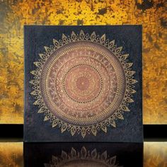 a black and gold wall hanging with a circular design on it's side, reflecting in the water